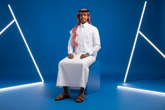 رجل سعودي بالثوب التقليدي يجلس في استوديو نيون أزرق