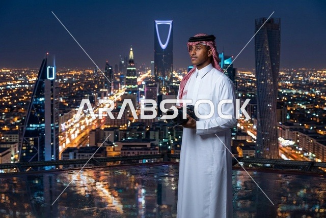 مصور سعودي بالزي التقليدي أمام أفق مدينة الرياض ليلا