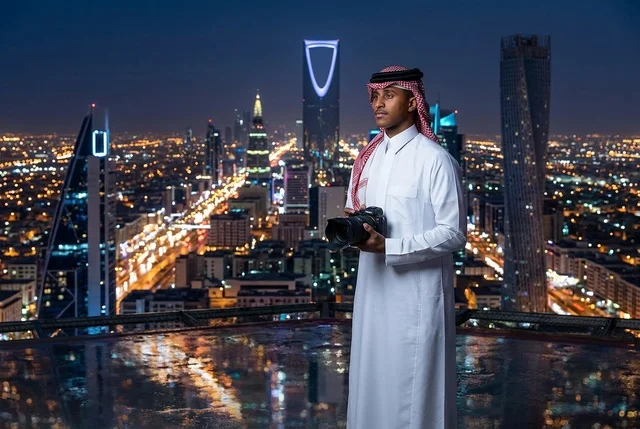 مصور سعودي بالزي التقليدي أمام أفق مدينة الرياض ليلا