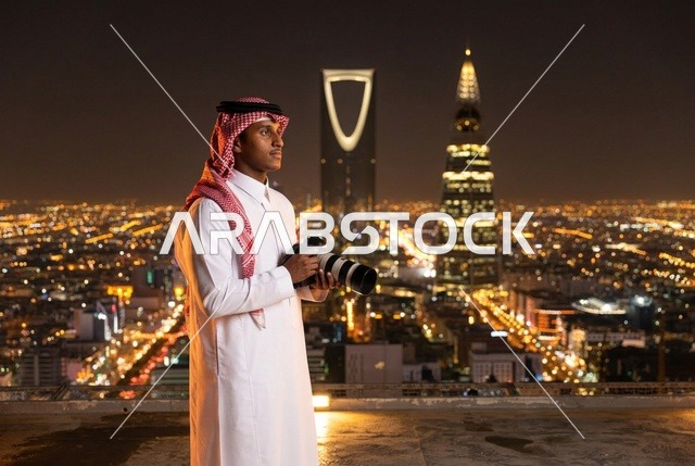 مصور سعودي يحمل كاميرا أمام أفق مدينة الرياض ليلا