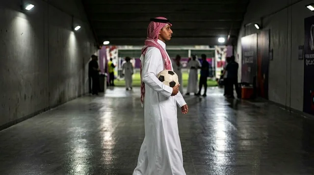 رجل سعودي بالثوب التقليدي يحمل كرة قدم في ممر الملعب