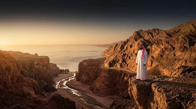 رجل سعودي بالزي التقليدي على حافة جبل وقت الغروب