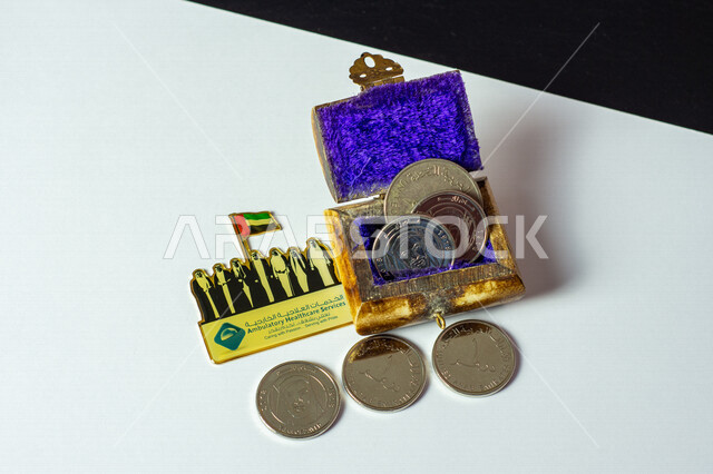 مجموعة من العملات النقدية من فئة الدرهم داخل صندوق أثري قديم مصورة على خلفية بيضاء ، عملات معدنية ، عملة دولة الإمارات العربية المتحدة ، الإحتفال باليوم الوطني الإماراتي ، شيوخ حكام دولة الإمارات السبع