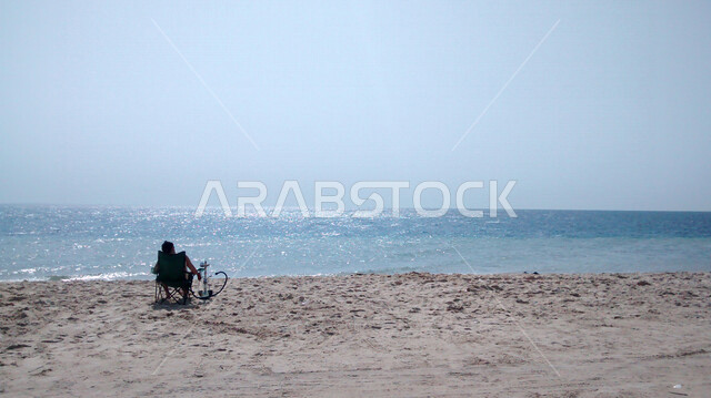 صورة جمالية لشاطئ نصف القمر في المنطقة الشرقية - الدمام بالمملكة العربية السعودية ، شواطئ الشرقية الساحرة ، أماكن سياحية ، الهافمون ويقع بالقرب من مدينة خبر فالمنطقة الشرقية من السعودية، زاوية من الخلف لرجل سائح جالس على شاطئ البحر