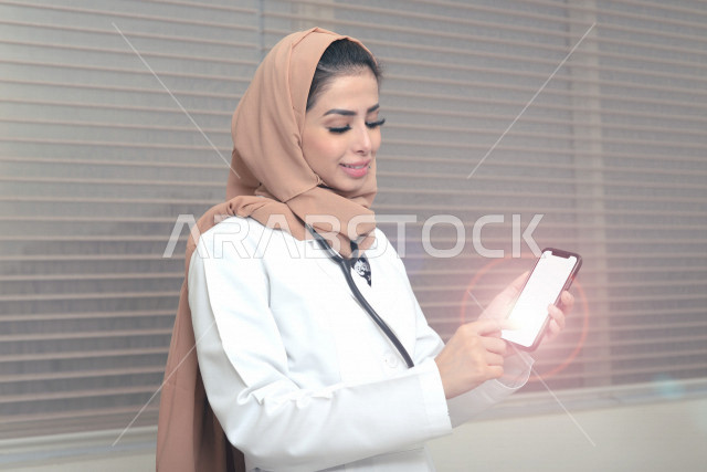 طبيبة عربية خليجية سعودية ترتدي المعطف الطبي و السماعة الطبية ،تستخدم الهاتف المحمول لتقديم الاستشارات الطبية عبر الانترنت ، تقديم الخدمات الصحية، العمل في القطاع الصحي ، مفهوم الطب والرعاية الصحية