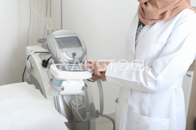 طبيبة عربية خليجية سعودية ترتدي المعطف الطبي وتستخدم جهاز الليزر ، اجهزة تقنية طبية حديثة ، تقديم الخدمات الصحية، طب الجلدية ومجال العناية بالبشرة