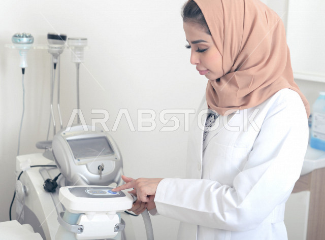 طبيبة عربية خليجية سعودية ترتدي المعطف الطبي وتستخدم جهاز الليزر ، اجهزة تقنية طبية حديثة ، تقديم الخدمات الصحية، طب الجلدية ومجال العناية بالبشرة