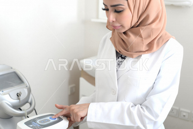 طبيبة عربية خليجية سعودية ترتدي المعطف الطبي وتستخدم جهاز الليزر ، اجهزة تقنية طبية حديثة ، تقديم الخدمات الصحية، طب الجلدية ومجال العناية بالبشرة