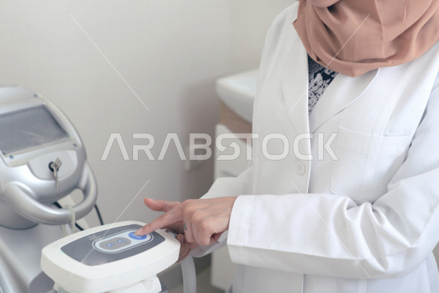 طبيبة عربية خليجية سعودية ترتدي المعطف الطبي وتستخدم جهاز الليزر ، اجهزة تقنية طبية حديثة ، تقديم الخدمات الصحية، طب الجلدية ومجال العناية بالبشرة