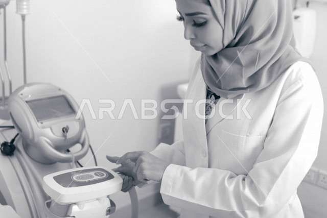 طبيبة عربية خليجية سعودية ترتدي المعطف الطبي وتستخدم جهاز الليزر ، اجهزة تقنية طبية حديثة ، تقديم الخدمات الصحية، طب الجلدية ومجال العناية بالبشرة