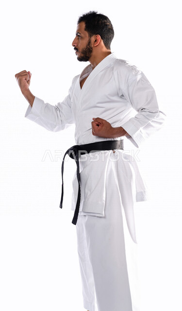 بورتريه بزاوية جانبية لرجل عربي خليجي سعودي يمارس رياضة الكاراتيه اليابانية، زي الكاراتيه الأبيض مع الحزام الأسود، التدرب على حركات قتالية خاصة، فنون قتالية يابانية، فنون الدفاع عن النفس، القوة البدنية، تطبيق حركات الكاتا، خلفية بيضاء