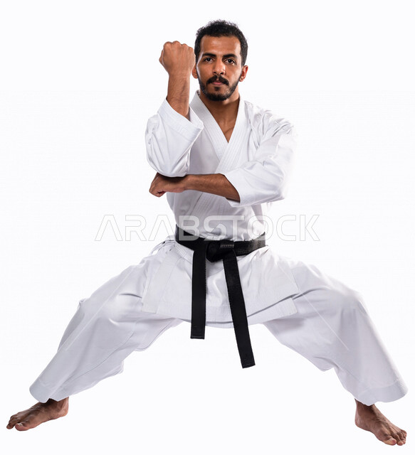 بورتريه لرجل عربي خليجي سعودي يمارس رياضة الكاراتيه اليابانية، زي الكاراتيه الأبيض مع الحزام الأسود، التدرب على حركات قتالية خاصة، فنون قتالية يابانية، فنون الدفاع عن النفس، القوة البدنية، تطبيق حركات الكاتا، خلفية بيضاء، صورة الجسم بالطول الكامل