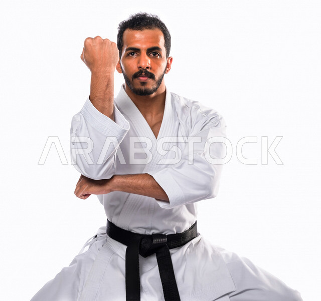 بورتريه لرجل عربي خليجي سعودي يمارس رياضة الكاراتيه اليابانية، زي الكاراتيه الأبيض مع الحزام الأسود، التدرب على حركات قتالية خاصة، فنون قتالية يابانية، فنون الدفاع عن النفس، القوة البدنية، تطبيق حركات الكاتا، خلفية بيضاء