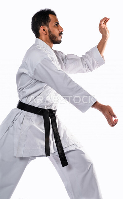 Portrait of a Saudi Arabian Gulf man practicing Japanese karate, white karate uniform with black belt, training in special combat movements, Japanese martial arts, martial arts, physical strength, kata movements, white background
