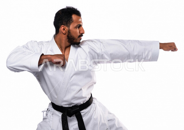 بورتريه لرجل عربي خليجي سعودي يمارس رياضة الكاراتيه اليابانية، زي الكاراتيه الأبيض مع الحزام الأسود، التدرب على حركات قتالية خاصة، فنون قتالية يابانية، فنون الدفاع عن النفس، القوة البدنية، تطبيق حركات الكاتا، خلفية بيضاء