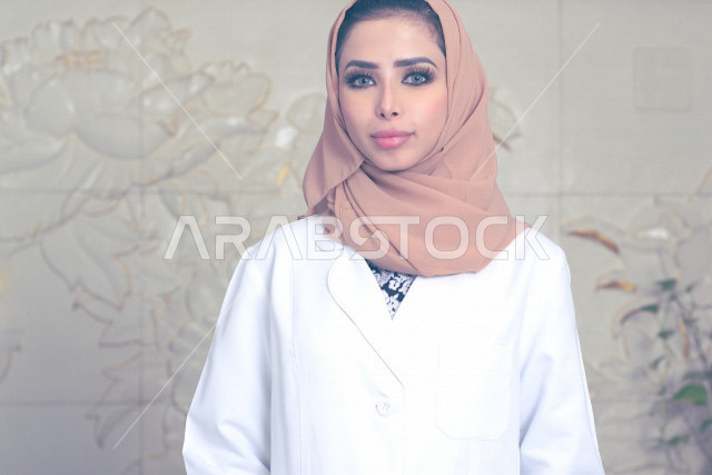 طبيبة عربية خليجية سعودية ترتدي المعطف الطبي وتنظر الى الكاميرا ، العمل في القطاع الصحي ،تقديم الخدمات الصحية، مفهوم الطب والرعاية الصحية