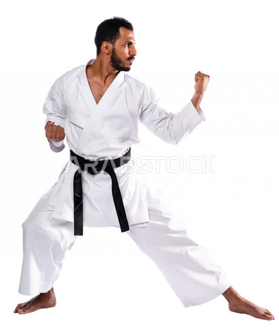 بورتريه لرجل عربي خليجي سعودي يمارس رياضة الكاراتيه اليابانية، زي الكاراتيه الأبيض مع الحزام الأسود، التدرب على حركات قتالية خاصة، فنون قتالية يابانية، فنون الدفاع عن النفس، القوة البدنية، تطبيق حركات الكاتا، خلفية بيضاء، صورة الجسم بالطول الكامل