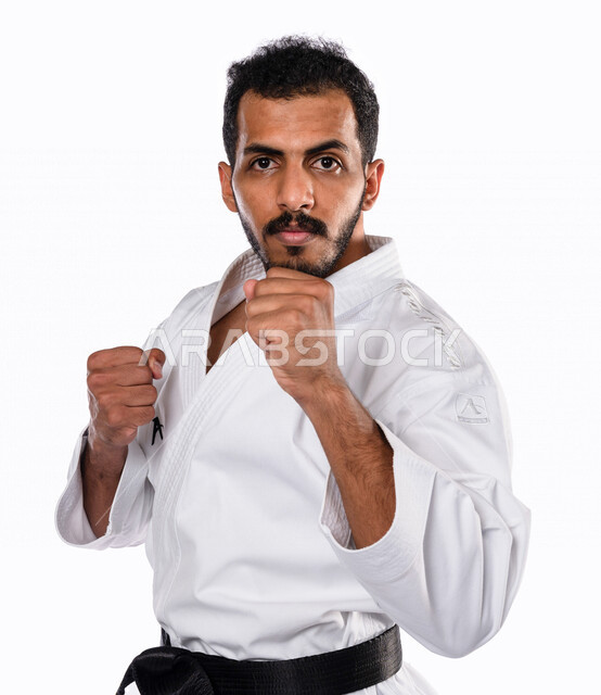 بورتريه لرجل عربي خليجي سعودي يمارس رياضة الكاراتيه اليابانية، زي الكاراتيه الأبيض مع الحزام الأسود، التدرب على حركات قتالية خاصة، فنون قتالية يابانية، فنون الدفاع عن النفس، القوة البدنية، تطبيق حركات الكاتا، خلفية بيضاء