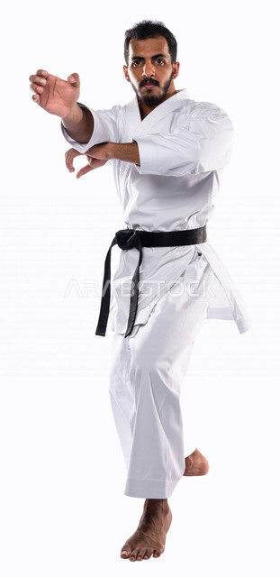 بورتريه لرجل عربي خليجي سعودي يمارس رياضة الكاراتيه اليابانية، زي الكاراتيه الأبيض مع الحزام الأسود، التدرب على حركات قتالية خاصة، فنون قتالية يابانية، فنون الدفاع عن النفس، القوة البدنية، تطبيق حركات الكاتا، خلفية بيضاء، صورة الجسم بالطول الكامل
