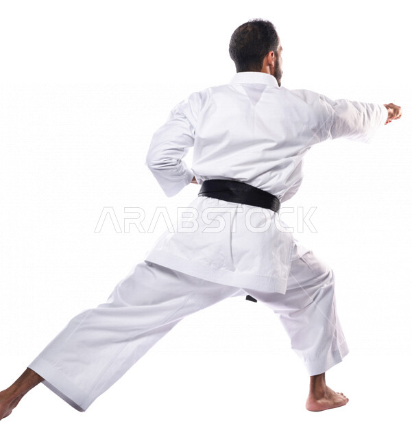 بورتريه من الخلف لرجل عربي خليجي سعودي يمارس رياضة الكاراتيه اليابانية، زي الكاراتيه الأبيض مع الحزام الأسود، التدرب على حركات قتالية خاصة، فنون قتالية يابانية، فنون الدفاع عن النفس، القوة البدنية، تطبيق حركات الكاتا، خلفية بيضاء، صورة الجسم بالطول الكامل