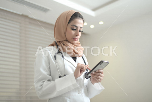 طبيبة عربية خليجية سعودية ترتدي المعطف الطبي و السماعة الطبية ،تستخدم الهاتف المحمول لتقديم الاستشارات الطبية عبر الانترنت ، تقديم الخدمات الصحية، العمل في القطاع الصحي ، مفهوم الطب والرعاية الصحية