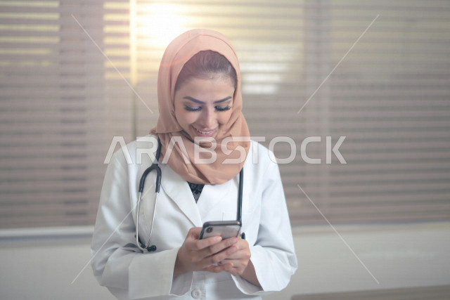 طبيبة عربية خليجية سعودية ترتدي المعطف الطبي و السماعة الطبية ،تستخدم الهاتف المحمول لتقديم الاستشارات الطبية عبر الانترنت ، تقديم الخدمات الصحية، العمل في القطاع الصحي ، مفهوم الطب والرعاية الصحية