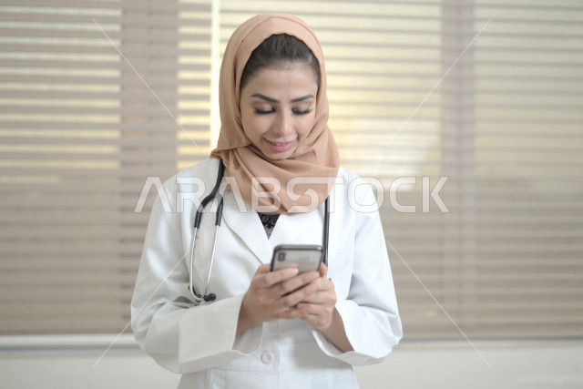 طبيبة عربية خليجية سعودية ترتدي المعطف الطبي و السماعة الطبية ،تستخدم الهاتف المحمول لتقديم الاستشارات الطبية عبر الانترنت ، تقديم الخدمات الصحية، العمل في القطاع الصحي ، مفهوم الطب والرعاية الصحية
