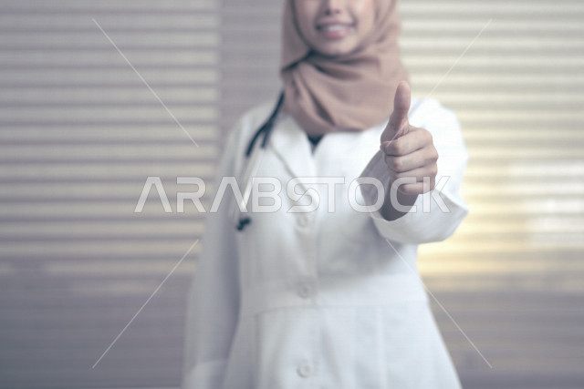 طبيبة عربية خليجية سعودية ترتدي المعطف الطبي و السماعة الطبية ،ترفع اصبع الابهام لاعلى لاعجابها بشيء ما ، العمل في القطاع الصحي ، تقديم الاستشارات الطبية والخدمات الصحية، مفهوم الطب والرعاية الصحية