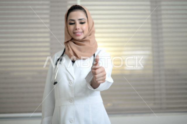 طبيبة عربية خليجية سعودية ترتدي المعطف الطبي و السماعة الطبية ،ترفع اصبع الابهام لاعلى لاعجابها بشيء ما ، العمل في القطاع الصحي ، تقديم الاستشارات الطبية والخدمات الصحية، مفهوم الطب والرعاية الصحية