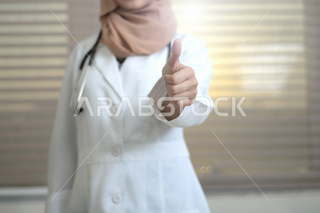طبيبة عربية خليجية سعودية ترتدي المعطف الطبي و السماعة الطبية ،ترفع اصبع الابهام لاعلى لاعجابها بشيء ما ، العمل في القطاع الصحي ، تقديم الاستشارات الطبية والخدمات الصحية، مفهوم الطب والرعاية الصحية