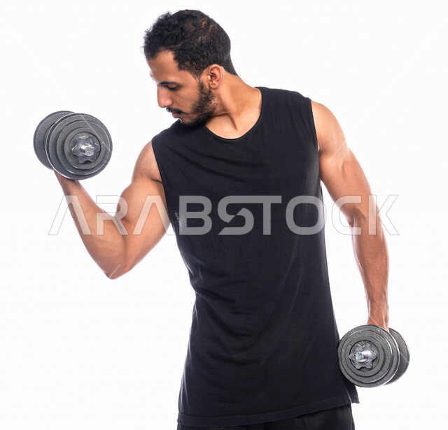 Portrait of a Saudi Arabian Gulf youth doing aerobic exercise with dumbbells, physical activity to maintain health and physical fitness, strengthening and building body muscles, weight lifting exercises (dumbbells), lifting heavy iron weights, bodybuildin
