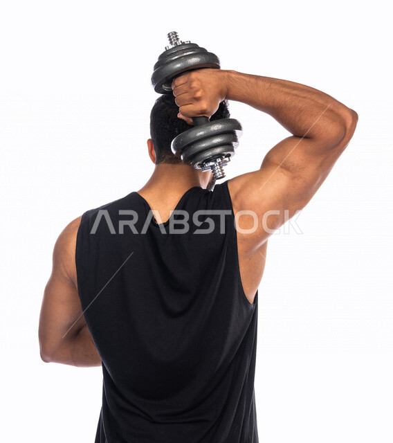 بورتريه من الخلف لشاب عربي خليجي سعودي يقوم بممارسة التمارين الرياضية مع الدمبل ، نشاط بدني للمحافظة على الصحة و اللياقة الجسدية ، تقوية عضلات الجسم و بنائها ، تمارين رفع الأثقال (دمبلز)، رفع الأوزان الحديدية الثقيلة ، كمال الأجسام ، لياقة و رشاقة