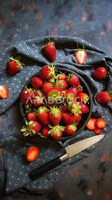 صورة مقربة من أعلى لطبق يحتوى على حبات الفراولة اللذيذة محاط بقطعة قماش عليها حبات من فواكه الفراولة و سكين للتقطيع ، فاكهه على شكل قلوب حمراء ، فاكهة الملوك ، طبق صحي
