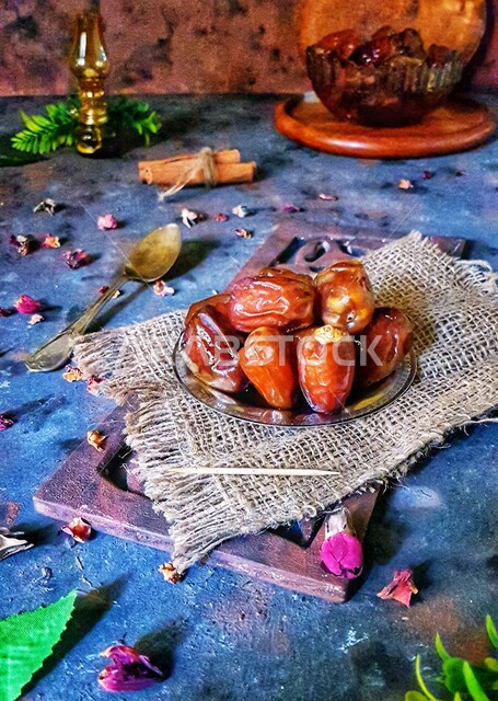 صورة مقربة لطبق من التمر الصحي على طاولة  ، مجموعة من أوراق الورد المتناثرة ، وجبة ذات قيمة غذائية عالية ، ضيافة رمضانية 