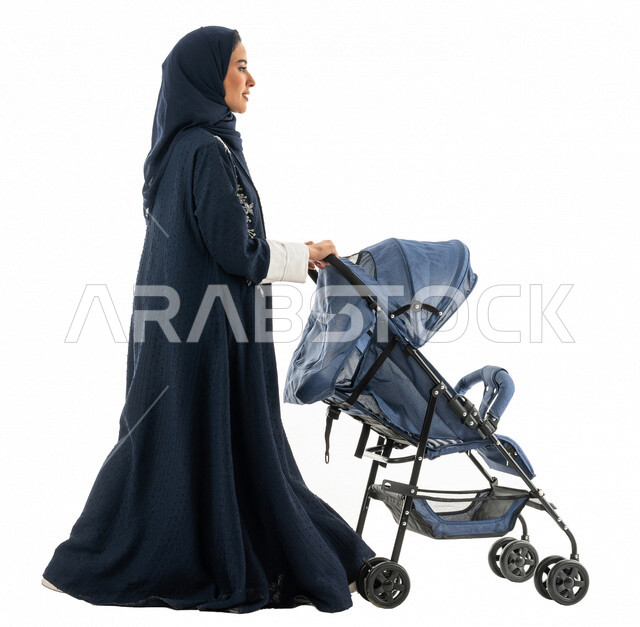 بورتريه لسيدة عربية خليجية سعودية تجر بيدها عربة الطفل ، الاهتمام بالاطفال ورعايتهم ، الاستمتاع بالتسوق والتنزه ، التجول والترفيه ، رحلة عائلية ممتعة ، صورة بالطول الكامل ، كامل الجسم