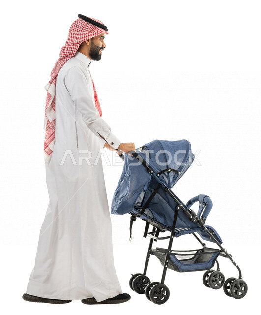 بورتريه لرجل عربي خليجي سعودي يرتدي الزي الخليجي التقليدي يجر بيده عربة الطفل ، الاهتمام بالاطفال ورعايتهم ، التجول والترفيه ، رحلة عائلية ممتعة ، صورة بالطول الكامل ، كامل الجسم