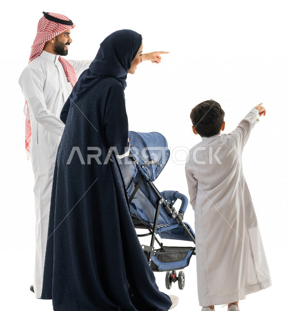 بورتريه لعائلة عربية خليجية سعودية تجر عربة الطفل وتشير بيدها لهدف ما ، التجول والترفيه ، الاستمتاع بالتسوق والتنزه ،رحلة عائلية ممتعة ، صورة بالطول الكامل ، كامل الجسم