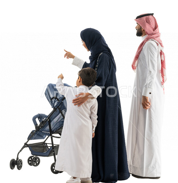 بورتريه لعائلة عربية خليجية سعودية تجر عربة الطفل وتشير بيدها لهدف ما ، التجول والترفيه ، الاستمتاع بالتسوق والتنزه ،رحلة عائلية ممتعة ، صورة بالطول الكامل ، كامل الجسم