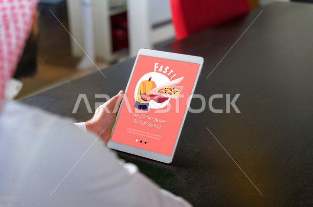 رجل عربي خليجي سعودي يستخدم تطبيقات الديلفري من خلال التابليت، تصفح تطبيقات المطاعم، تطبيق ديلفري لطلب الطعام من خلال التابليت، خدمة توصيل الطعام، تطبيقات الديلفري، استخدام التقنيات الحديثة في طلب الطعام