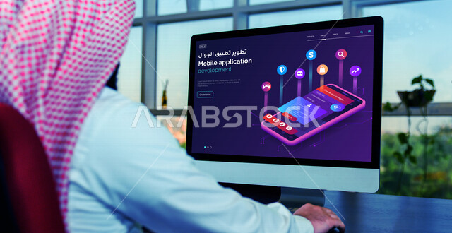 رجل عربي خليجي سعودي يجلس أمام شاشة الحاسوب ويتصفح موقع الكتروني خاص بتطوير تطبيقات الجوال، خدمة تطوير وبناء تطبيقات الجوال، تصفح مواقع الانترنت، العمل عن بعد، الواجهة الامامية للموقع الالكتروني، استخدام التقنيات الحديثة في تطوير تطبيقات الجوال