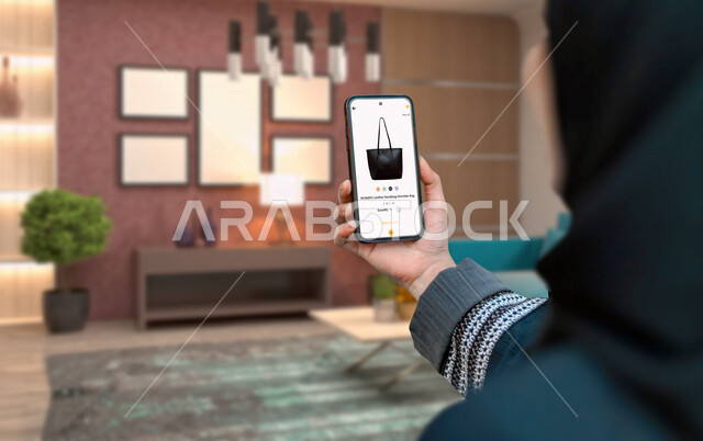 امرأة عربية خليجية سعودية تستخدم الهاتف المحمول في تصفح التطبيقات التجارية، التسوق الإلكتروني، خدمة تطبيقات التسوق الإلكترونية، شراء المنتجات من خلال الانترنت، التطبيقات تجارية، استخدام التقنيات الحديثة في شراء المنتجات والسلع عبر الانترنت