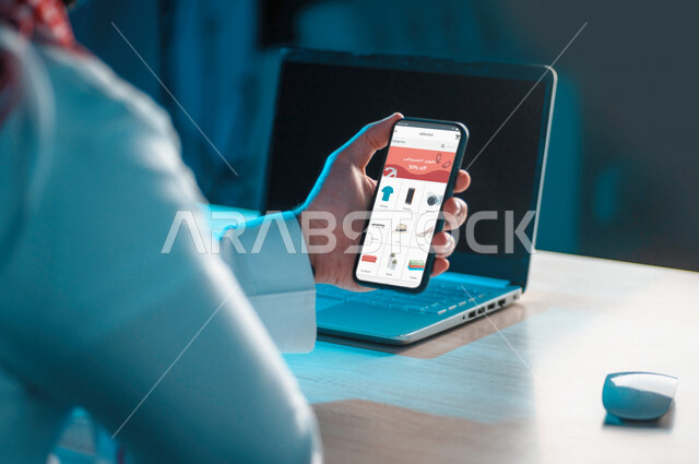 رجل عربي خليجي سعودي يستخدم الهاتف المحمول في تصفح التطبيقات التجارية، التسوق الإلكتروني، خدمة تطبيقات التسوق الإلكترونية، شراء المنتجات من خلال الانترنت، التطبيقات تجارية، استخدام التقنيات الحديثة في شراء المنتجات والسلع عبر الانترنت