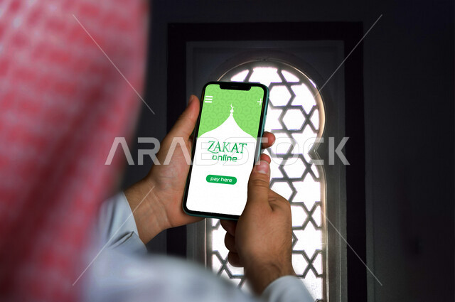 رجل عربي خليجي سعودي يستخدم تطبيق زكاة اونلاين من خلال الهاتف المحمول، خدمة تطبيق الزكاة على الجوال، استخدام التقنيات الحديثة في العبادة والتقرب الى الله، استخدام تقنيات حديثة، تطبيق زكاة اونلاين، تطبيقات اسلامية