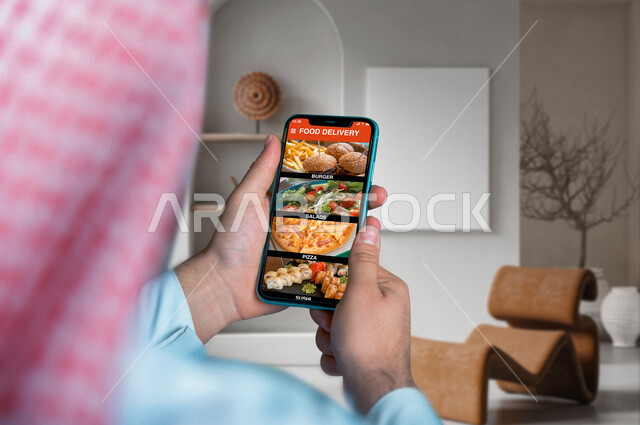 A Saudi Arabian Gulf man uses delivery applications through a mobile phone, browse restaurant applications, mobile food ordering application, food delivery service, delivery applications, using modern technologies in ordering food