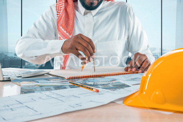 مهندس عربي خليجي سعودي داخل مكتب هندسي قوم باستخدام فرجار هندسي ، إستخدام جهاز الحاسوب المحمول لمتابعة الأعمال و المهام الهندسية ، إستخدام أدوات و معدات هندسية ، مخطط تصميم هندسي ، مهن و وظائف ، مهندس معماري محترف