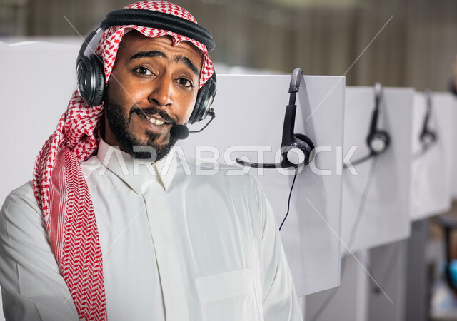 رجل عربي خليجي سعودي يرتدي الزي السعودي التقليدي يضع سماعات الرأس الصوتية بإيماءات وجه ويدين مختلفة ، العمل بالدعم الفني ، الإستعلامات والإستفسارات  ،الاجابة على أسئلة العملاء  ، خدمة العملاء والدعم الفني