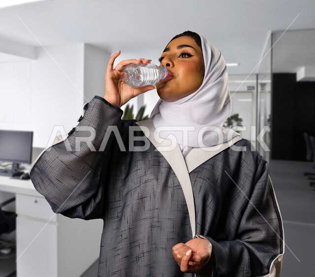 سيدة عربية خليجية سعودية تقوم بشرب المياه من زجاجة ماء بلاستيكية صغيرة ، المداومة على شرب المياه ، صحة و لياقة ، المحافظة على سلامة الجهاز المناعي للجسم 