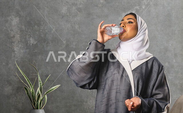 سيدة عربية خليجية سعودية تقوم بشرب المياه من زجاجة ماء بلاستيكية صغيرة ، المداومة على شرب المياه ، صحة و لياقة ، المحافظة على سلامة الجهاز المناعي للجسم 