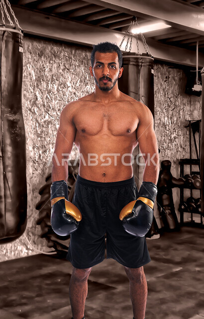 شاب عربي خليجي سعودي في النادي، يرتدي زي الملاكمة وقفازات الملاكمة، التدرب على حركات قتالية، فنون قتالية، رياضات القتال والدفاع عن النفس، الملاكمة والمصارعة، رياضة الملاكمة في السعودية، نادي رياضي رجالي، بطولات رياضة الملاكمة الرجالية