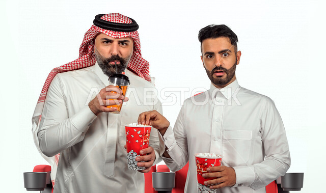 صديقان عربيان سعوديان خليجيان يستمتعان بوقت الفراغ , عطلة نهاية الأسبوع , مشاهدة الأفلام والعروض المسرحية في السنما , الاستمتاع بتناول الفشار أثناء مشاهدة الفلم , إيماءات وجه ويدين مختلفة , خلفية بيضاء .